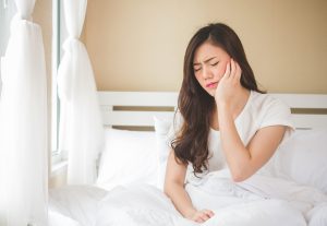 A woman sitting up in bed holding her cheek in pain